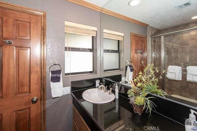 bathroom with visible vents, ornamental molding, a textured wall, vanity, and a shower with shower door