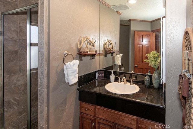 bathroom featuring crown molding, a textured wall, vanity, a shower stall, and visible vents