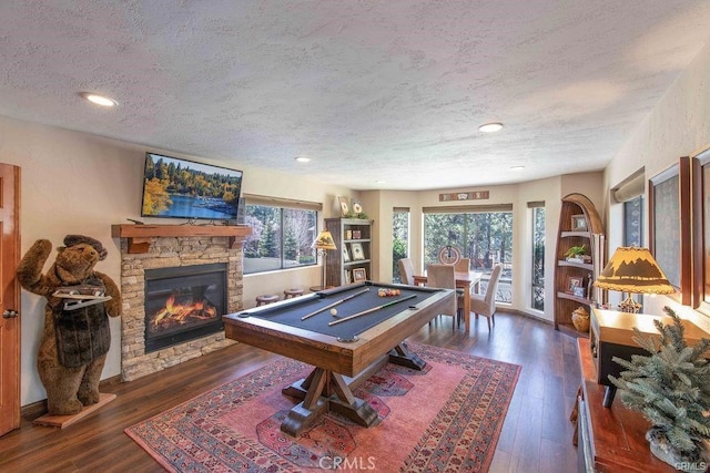 rec room featuring pool table, a stone fireplace, hardwood / wood-style flooring, and a textured ceiling