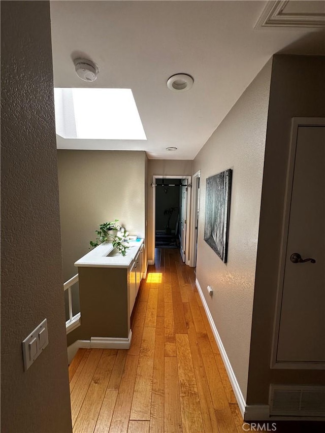 corridor featuring light wood-type flooring, baseboards, visible vents, and a skylight