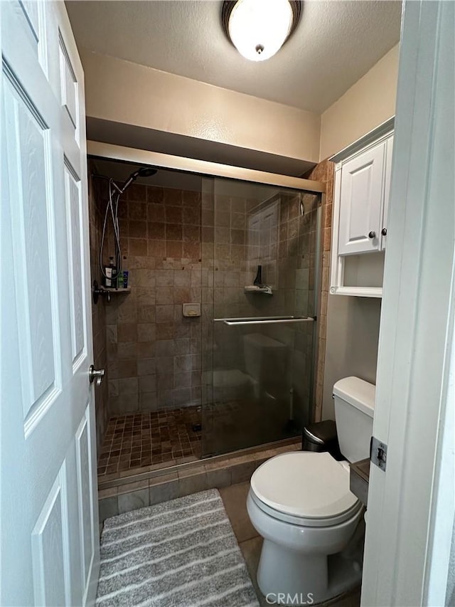 bathroom with toilet, a textured ceiling, tile patterned flooring, and a stall shower