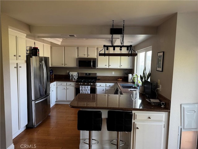 kitchen featuring appliances with stainless steel finishes, a sink, a peninsula, white cabinetry, and dark wood-type flooring