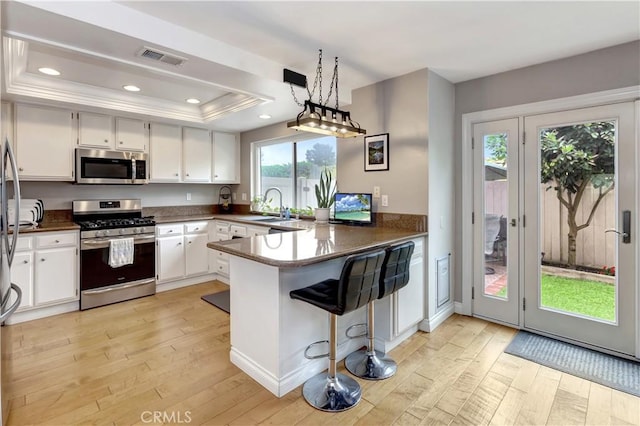 3 Holly Hill Ln, Laguna Hills, CA 92653 - kitchen with stainless steel appliances, a raised ceiling, a peninsula, light wood-style flooring, and white cabinets