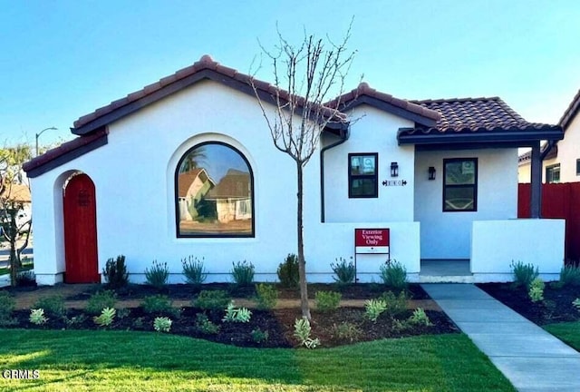 mediterranean / spanish home with stucco siding, a tile roof, and a front yard