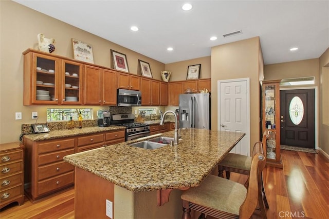 9169 Wooded Hill Dr, Corona, CA 92883 - kitchen featuring brown cabinetry, a breakfast bar, a sink, light wood finished floors, and stainless steel appliances