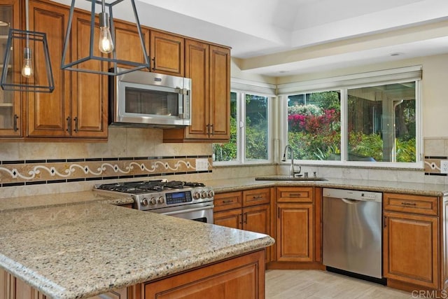 kitchen featuring brown cabinets, light stone countertops, a sink, stainless steel appliances, and a peninsula