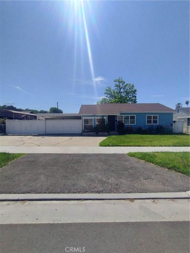 ranch-style house featuring concrete driveway, fence, and a front lawn