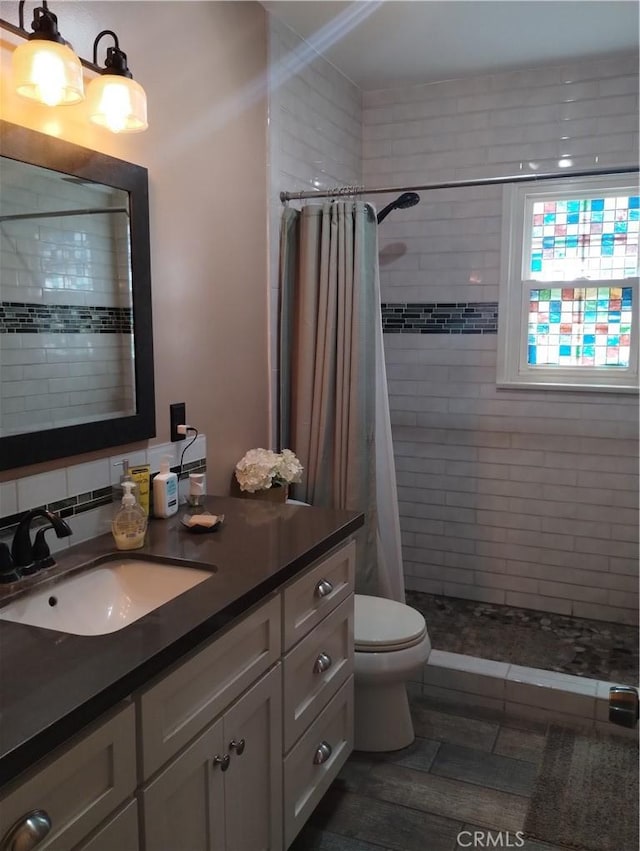 bathroom featuring vanity, a tile shower, and toilet