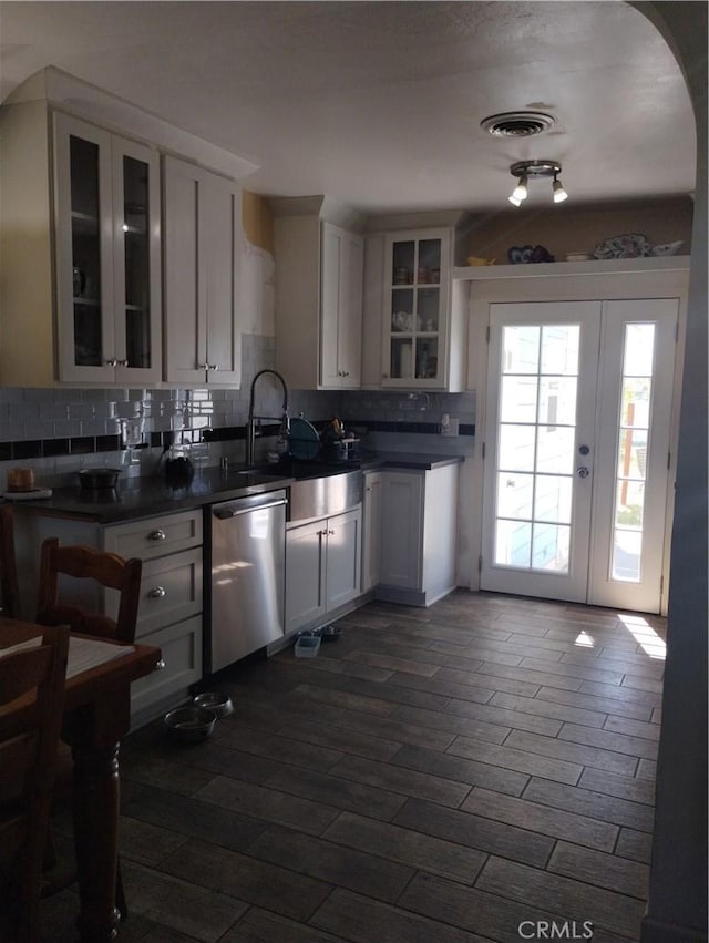 kitchen with stainless steel dishwasher, dark countertops, glass insert cabinets, tasteful backsplash, and dark wood finished floors