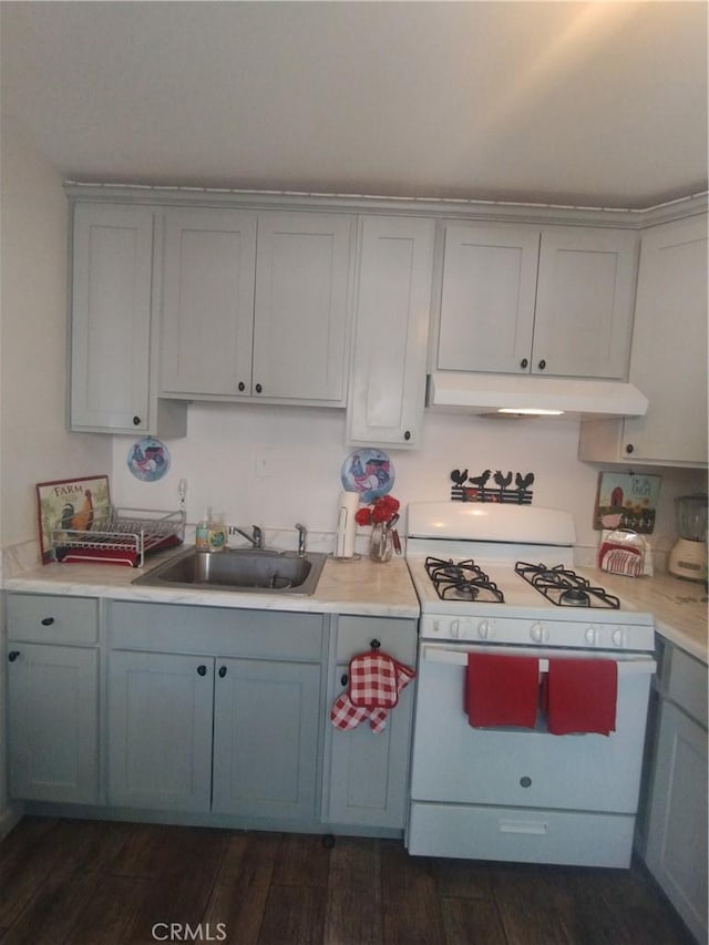 kitchen with a sink, light countertops, gray cabinetry, under cabinet range hood, and white range with gas stovetop