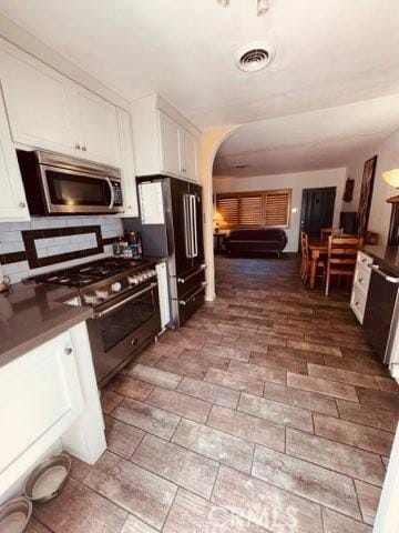 3620 Hoover St, Riverside, CA 92504 - kitchen with high end appliances, white cabinetry, dark countertops, arched walkways, and backsplash