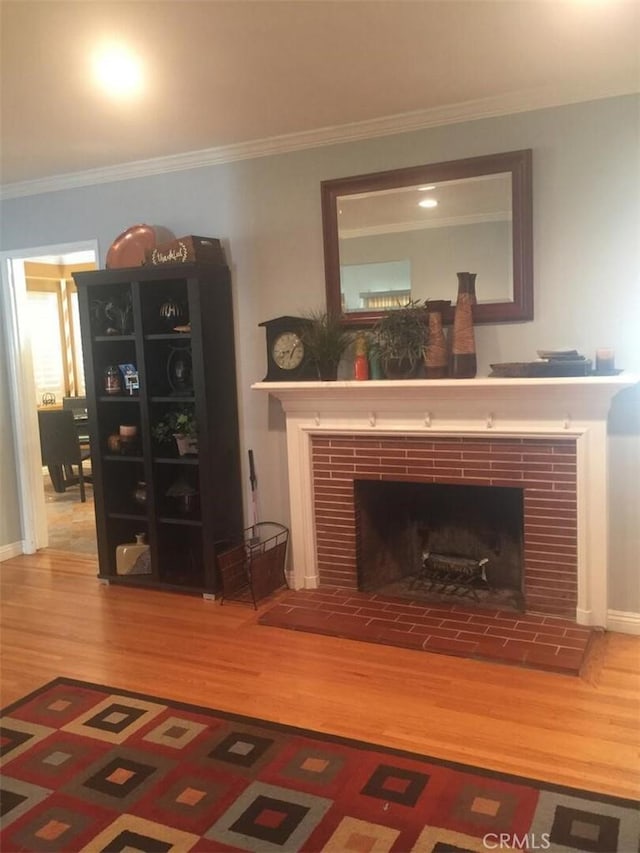 living area with a fireplace, crown molding, baseboards, and wood finished floors