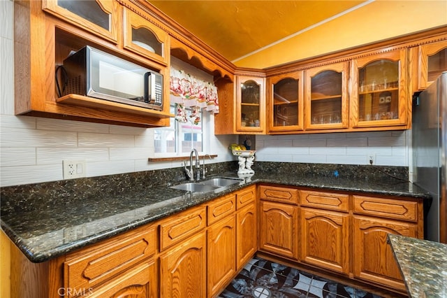 kitchen with brown cabinetry, freestanding refrigerator, a sink, backsplash, and vaulted ceiling