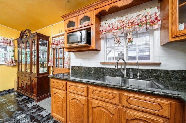 kitchen with decorative backsplash, stainless steel microwave, brown cabinetry, and a sink