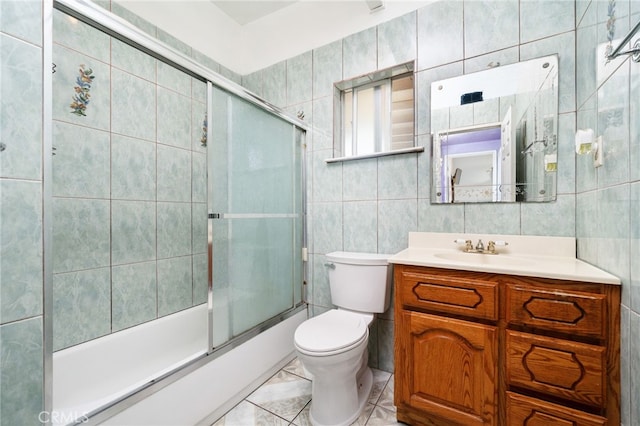 full bath featuring vanity, bath / shower combo with glass door, toilet, and tile walls