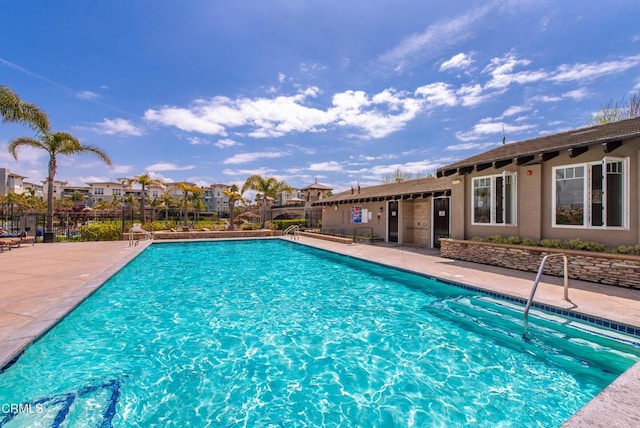 community pool with a patio area, fence, and a residential view