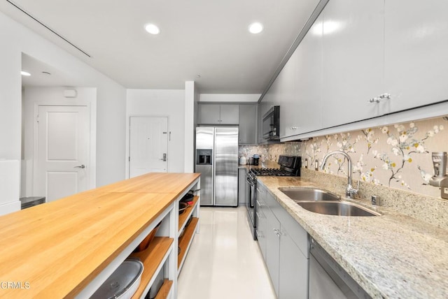 kitchen featuring decorative backsplash, gray cabinets, light stone counters, a sink, and stainless steel appliances