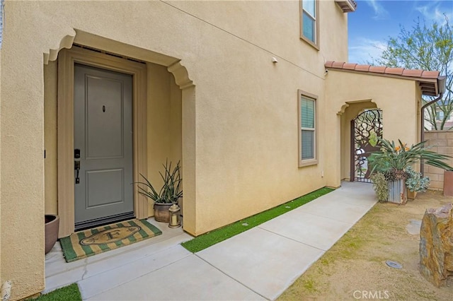 view of exterior entry with fence and stucco siding