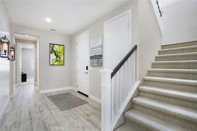 foyer entrance featuring baseboards, stairs, wood finished floors, and visible vents