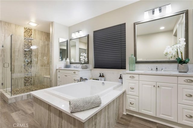 full bathroom featuring a shower stall, wood finished floors, a bath, and vanity