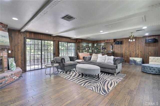 living area featuring wood-type flooring, beamed ceiling, wood walls, and visible vents