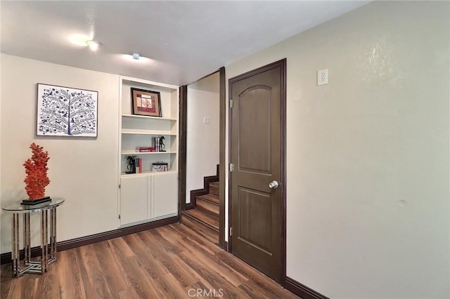 hall featuring stairs, dark wood-style flooring, baseboards, and built in shelves
