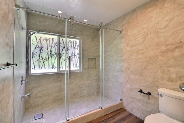 bathroom featuring toilet, recessed lighting, tile walls, wood finished floors, and a stall shower