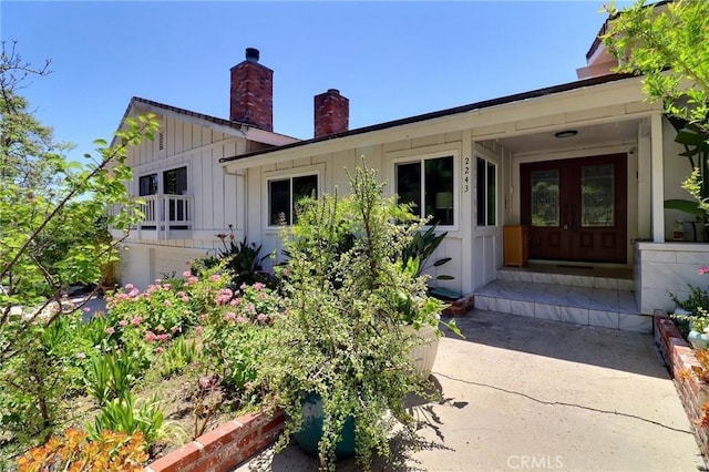 view of front facade with board and batten siding, french doors, and a chimney