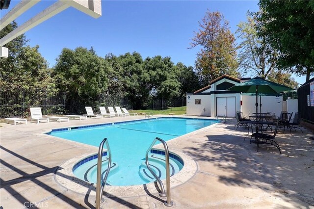 pool featuring a patio, an outdoor structure, a community hot tub, and fence