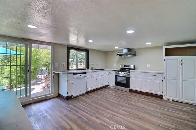 kitchen featuring dark wood-style flooring, gas range, dishwasher, a sink, and wall chimney exhaust hood