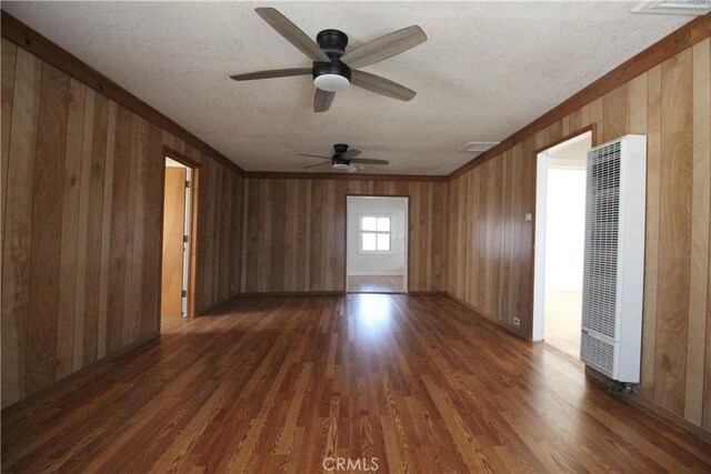 200 E St, Taft, CA 93268 - unfurnished room featuring a ceiling fan, dark wood-style flooring, a textured ceiling, wooden walls, and a heating unit