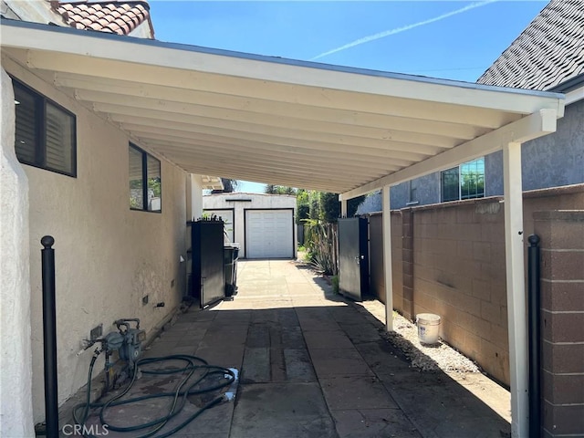 view of patio / terrace featuring fence, an outbuilding, and an attached carport