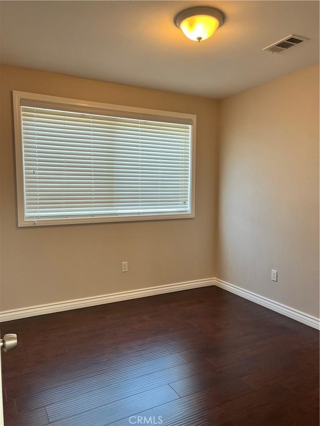 unfurnished room with baseboards, dark wood-style flooring, and visible vents