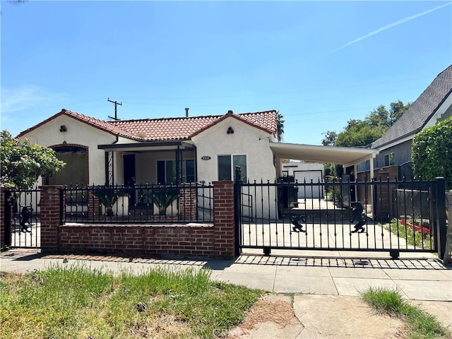 mediterranean / spanish-style home with a fenced front yard, a tile roof, stucco siding, a gate, and an attached carport