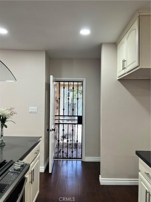 kitchen with stainless steel range with gas stovetop, baseboards, dark wood-style floors, and dark countertops