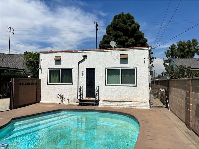 rear view of house featuring a fenced in pool, stucco siding, and fence