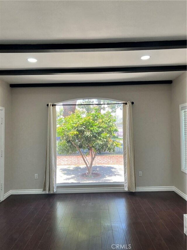 spare room featuring baseboards, dark wood-style floors, and beam ceiling