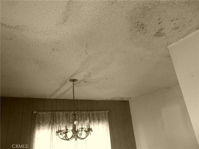 details featuring a textured ceiling, a chandelier, and wooden walls