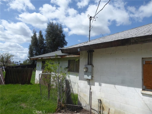 view of property exterior with fence, a shingled roof, and concrete block siding
