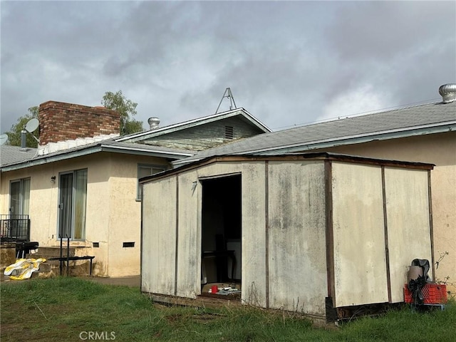 rear view of house featuring stucco siding, an outbuilding, a chimney, and a storage unit