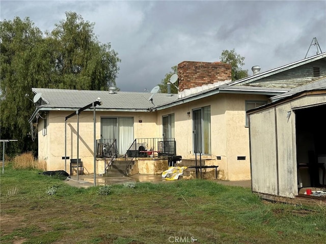 rear view of house featuring a yard, a chimney, a storage shed, and stucco siding