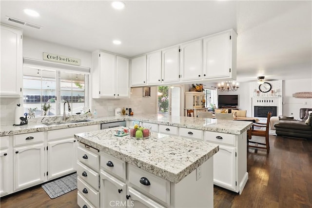 kitchen with a peninsula, a center island, a sink, a brick fireplace, and visible vents