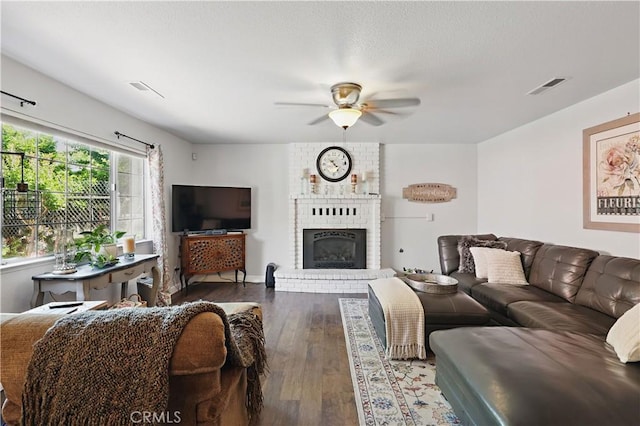 living area with a fireplace, ceiling fan, wood-type flooring, and visible vents