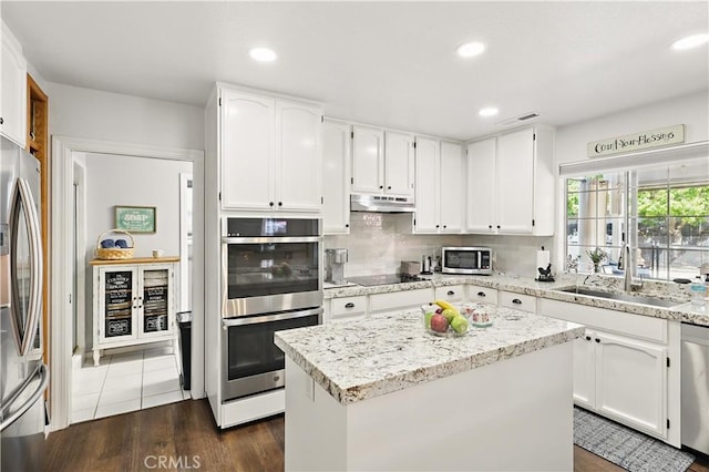3571 White Wolf Ct, Merced, CA 95340 - kitchen with appliances with stainless steel finishes, under cabinet range hood, a sink, white cabinetry, and decorative backsplash