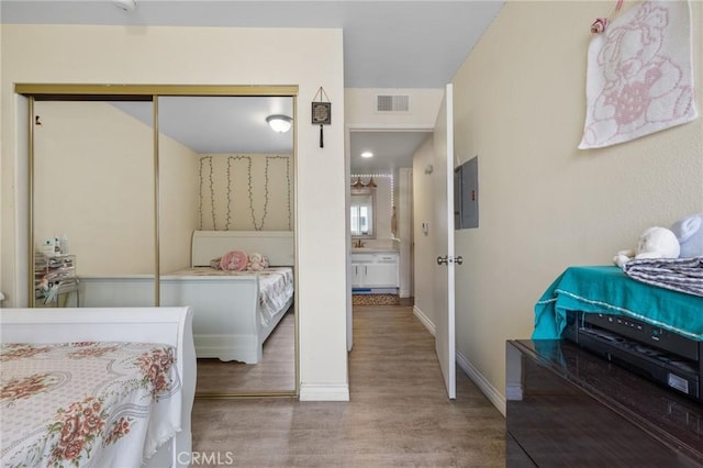 bedroom featuring electric panel, visible vents, wood finished floors, baseboards, and a closet