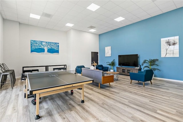 recreation room with a towering ceiling, baseboards, a drop ceiling, and light wood-style floors