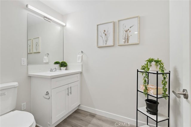 half bathroom featuring vanity, baseboards, toilet, and wood finished floors