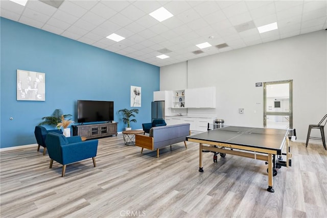 playroom with baseboards, light wood-style flooring, a high ceiling, and a paneled ceiling