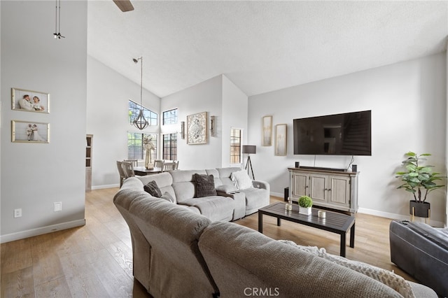 living area featuring baseboards, a high ceiling, light wood-type flooring, and a chandelier