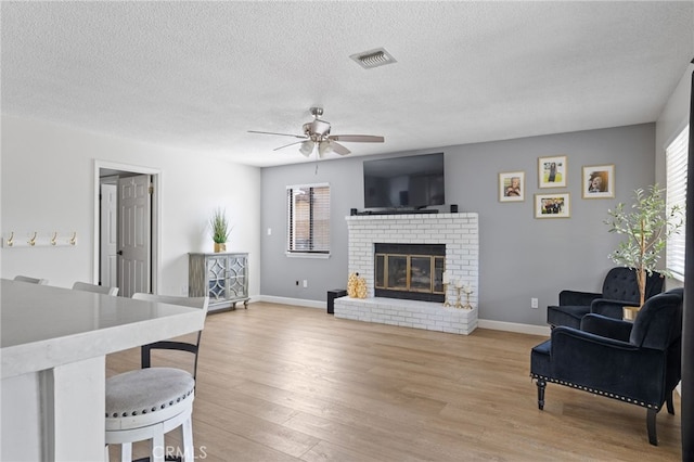 living area featuring a fireplace, a ceiling fan, baseboards, light wood-type flooring, and visible vents
